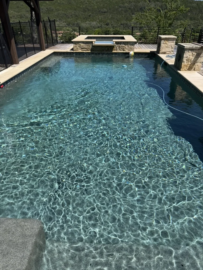 Sunlight rippling across a clear backyard pool with a stone spa and Hill Country views.