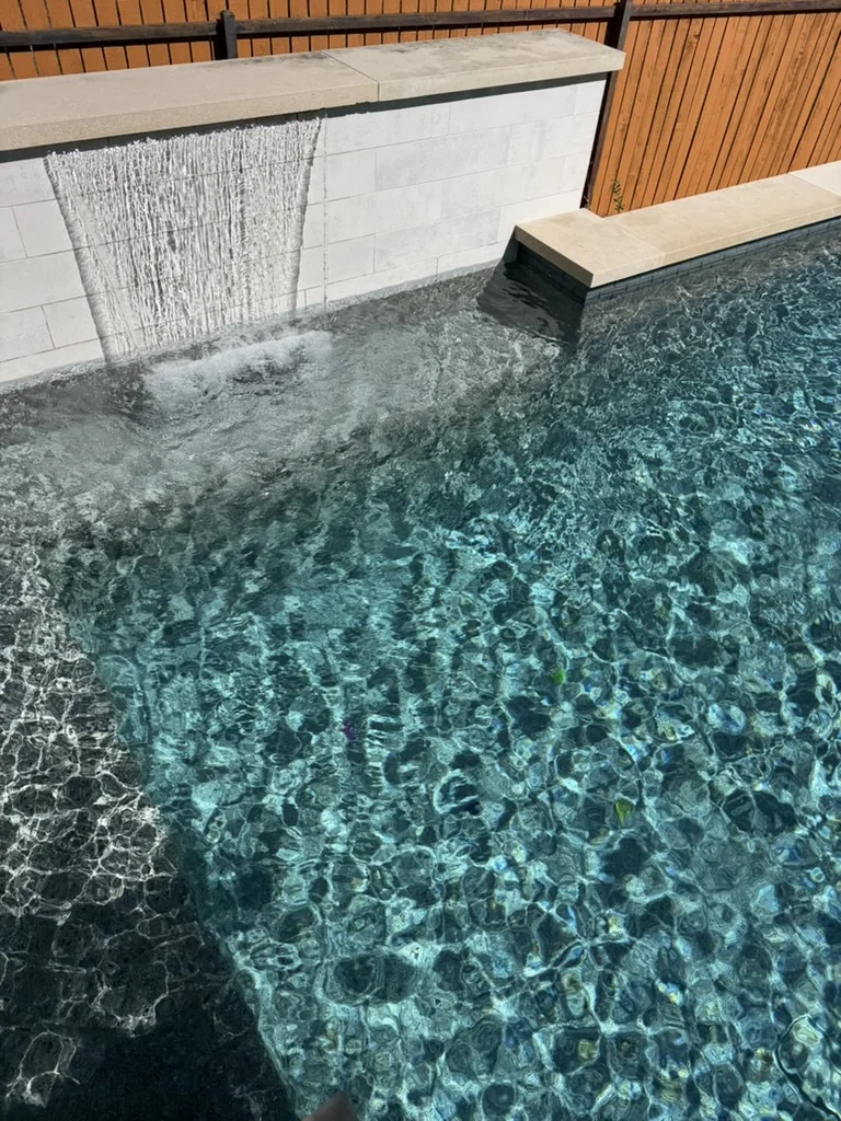 A stone waterfall flowing into sparkling blue pool water.